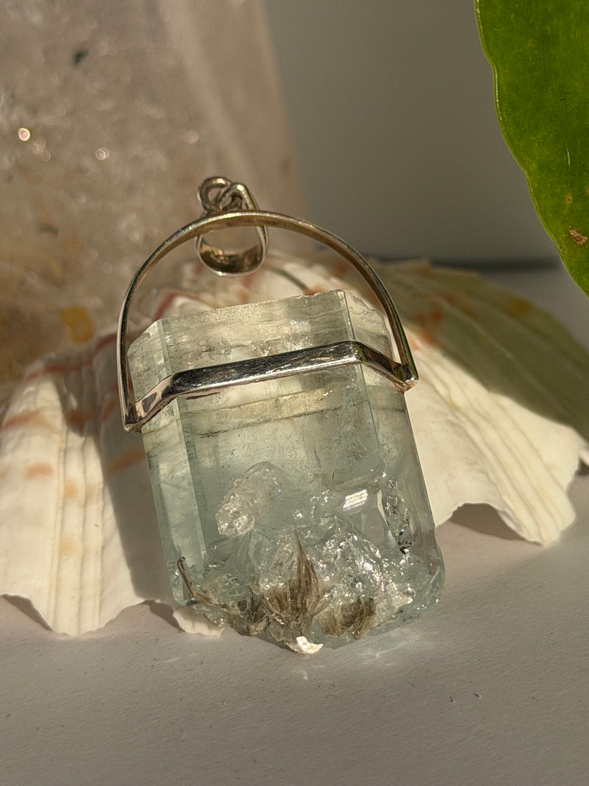 Aquamarine Crystal pendant with silver setting on a seashell in the sunlight