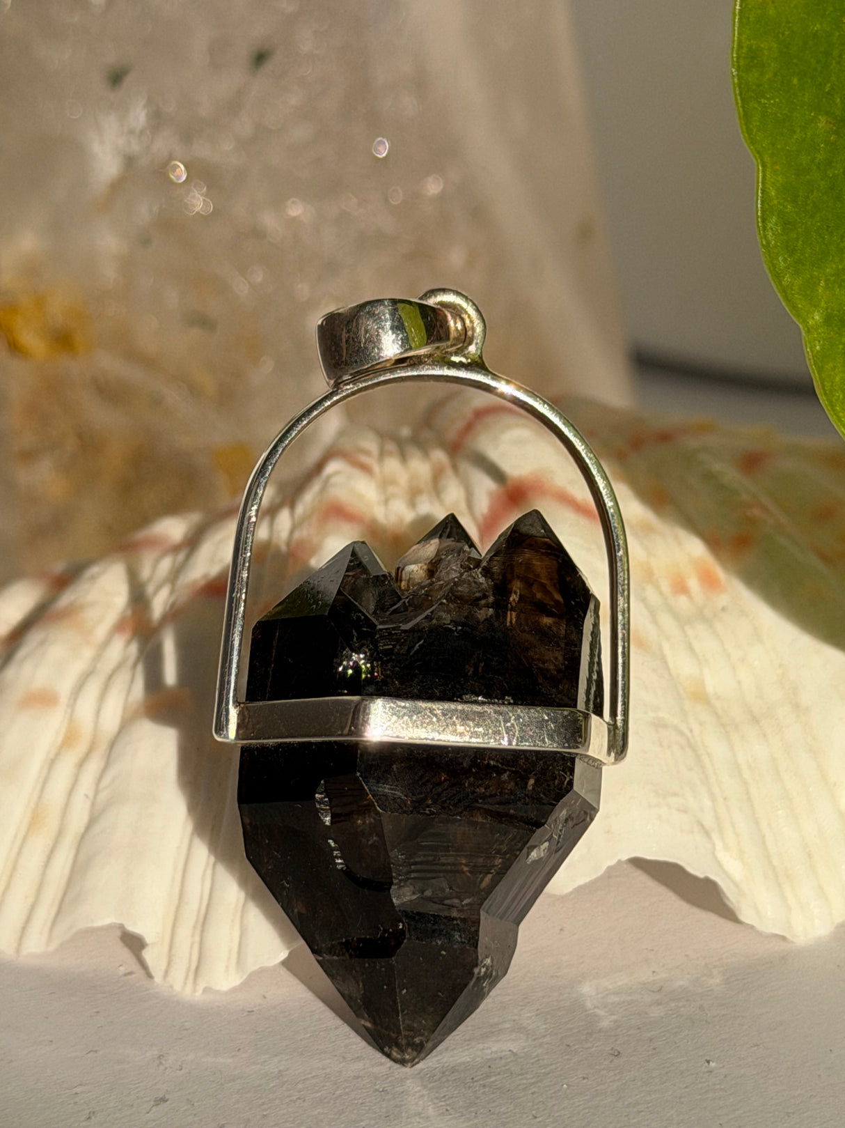 Mooralla Smokey Quartz crystal set into a silver pendant against a seashell