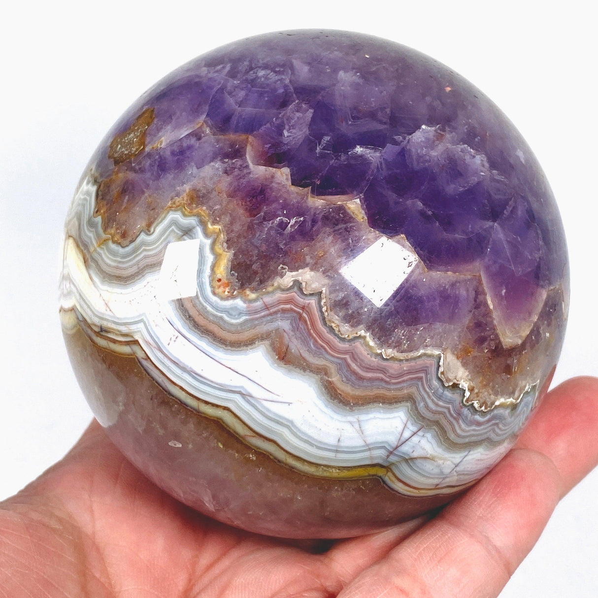 An Amethyst Agate sphere with banding patterns displayed in a hand.