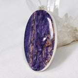 Purple Charoite large oval pendant in sterling silver sitting on a crystal cluster