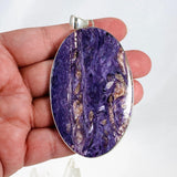 Purple Charoite large oval pendant in sterling silver sitting on a hand