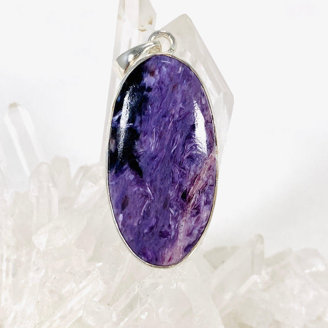 Purple Charoite oval pendant in sterling silver sitting on a crystal cluster