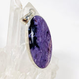 Purple Charoite oval pendant in sterling silver sitting on a crystal cluster