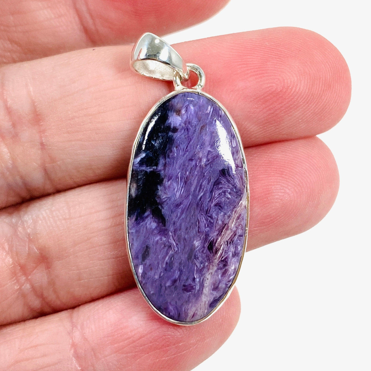 Purple Charoite oval pendant in sterling silver sitting on a hand
