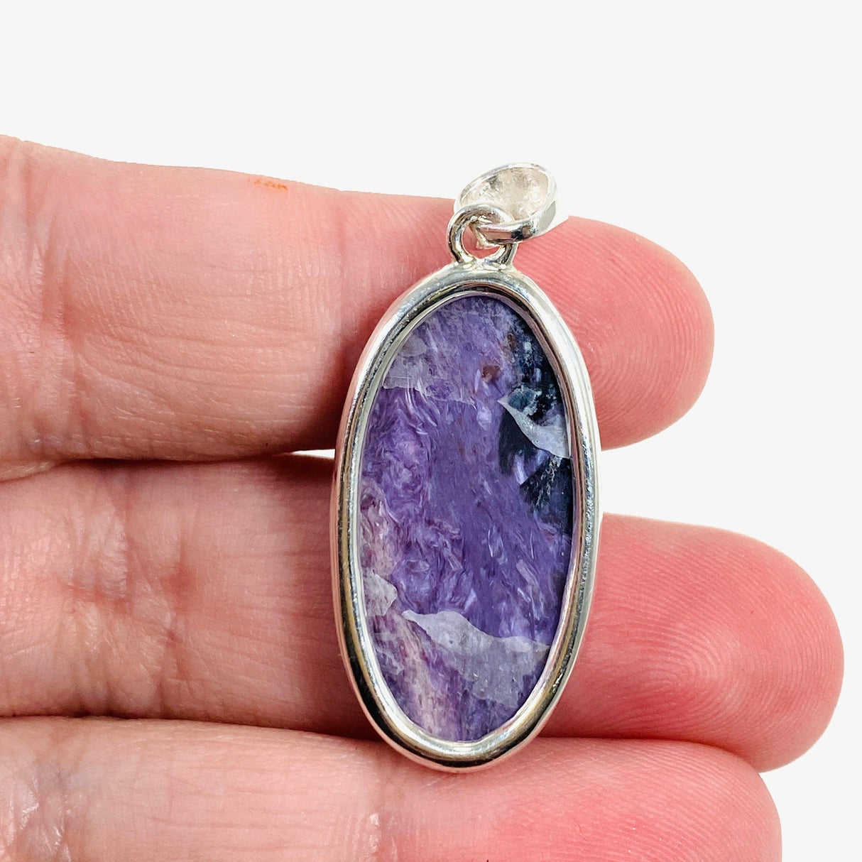 Purple Charoite oval pendant in sterling silver sitting on a hand