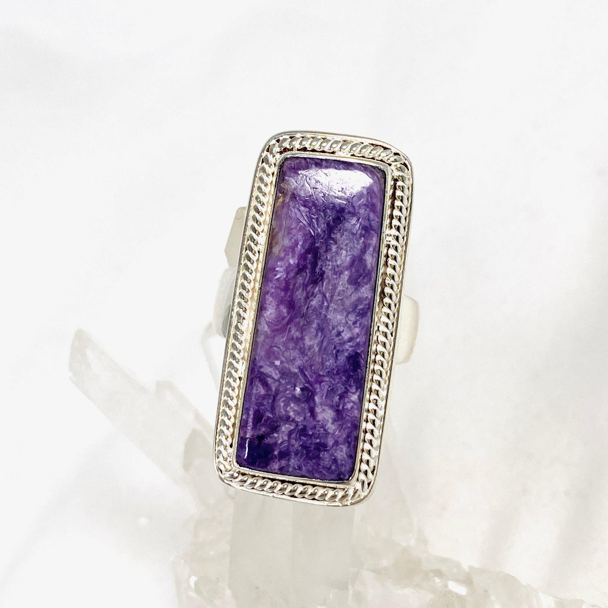 Purple Charoite rectangle ring in sterling silver sitting on a crystal cluster 