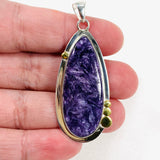 Purple Charoite tear drop pendant with brass detailing  in sterling silver sitting in a hand