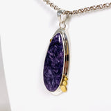Purple Charoite tear drop pendant with brass detailing  in sterling silver sitting on a chain