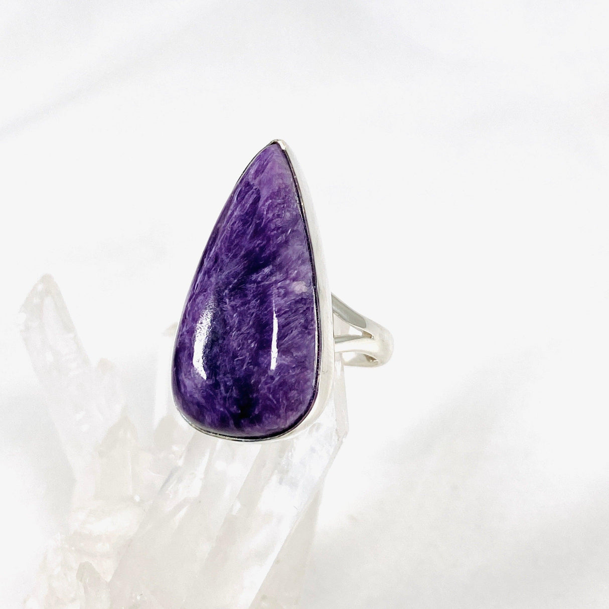 Purple Charoite tear drop ring in sterling silver sitting on a crystal cluster