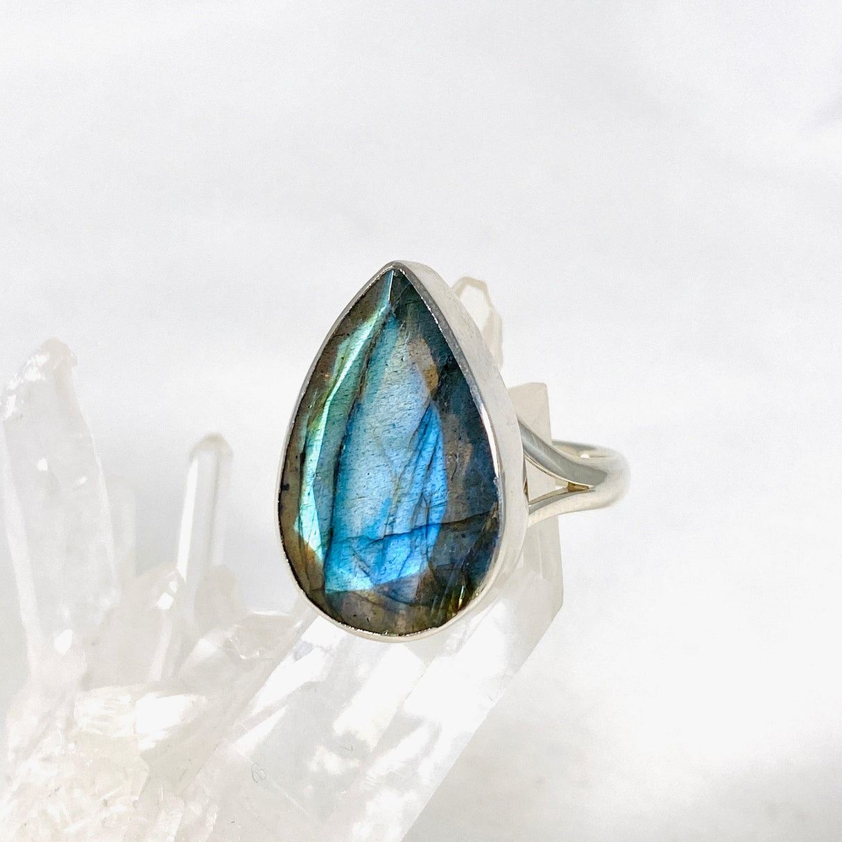 Blue iridescent Labradorite faceted gemstone and silver ring on a clear quartz crystal