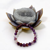 A bracelet featuring a series of round purple amethyst crystal beads on a clear elastic stretch cord