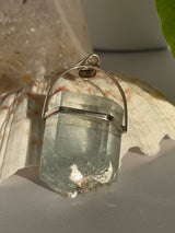 Aquamarine Crystal pendant with silver setting on a seashell in the sunlight