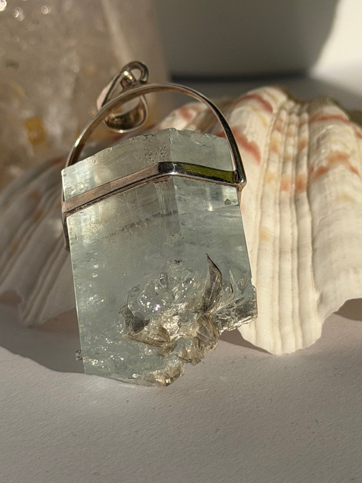 Aquamarine Crystal pendant with silver setting on a seashell in the sunlight