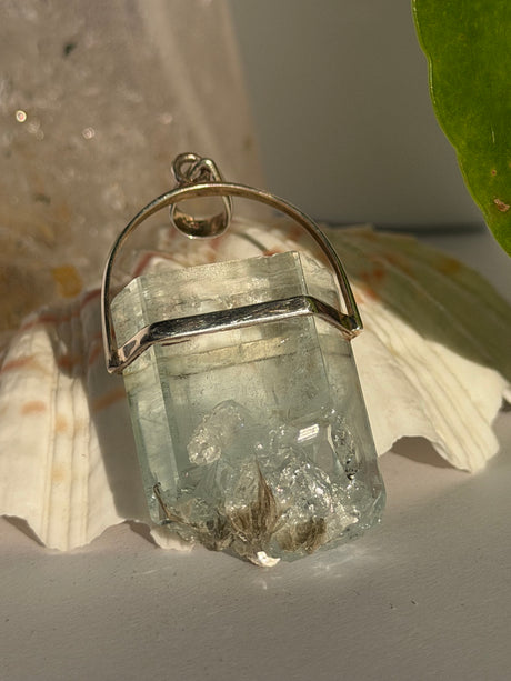 Aquamarine Crystal pendant with silver setting on a seashell in the sunlight