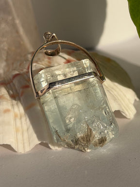 Aquamarine Crystal with muscovite pendant with silver setting on a seashell in the sunlight