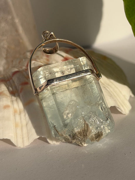 Aquamarine Crystal with muscovite pendant with silver setting on a seashell in the sunlight