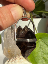 Mooralla Smokey Quartz crystal set into a silver pendant held in front of a crystal and plant