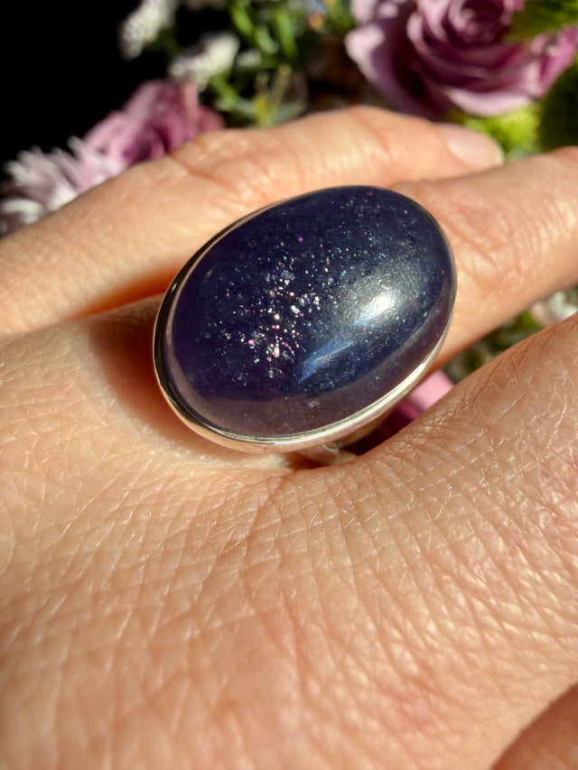 Sunstone in iolite oval cabochon ring worn on the hand, showing deep indigo-blue-violet tones with scattered sparkle and a bright glint across the stone
