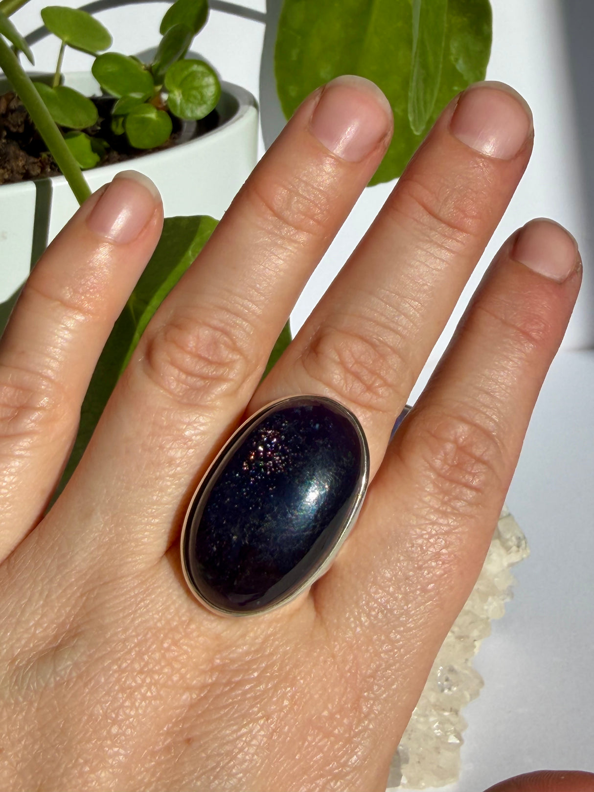 Sunstone in iolite oval ring worn on the hand, showing a concentrated cluster of pink and silver sparkle catching the light