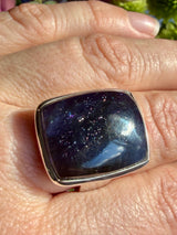 Sunstone in iolite rectangular cabochon ring worn on the hand, showing deep indigo-purple tones with a concentrated cluster of sparkle and a bright glint