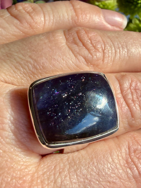 Sunstone in iolite rectangular cabochon ring worn on the hand, showing deep indigo-purple tones with a concentrated cluster of sparkle and a bright glint
