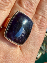 Sunstone in iolite rectangular cabochon ring worn on the hand, showing deep indigo-purple-black colour with fine scattered sparkle across the stone