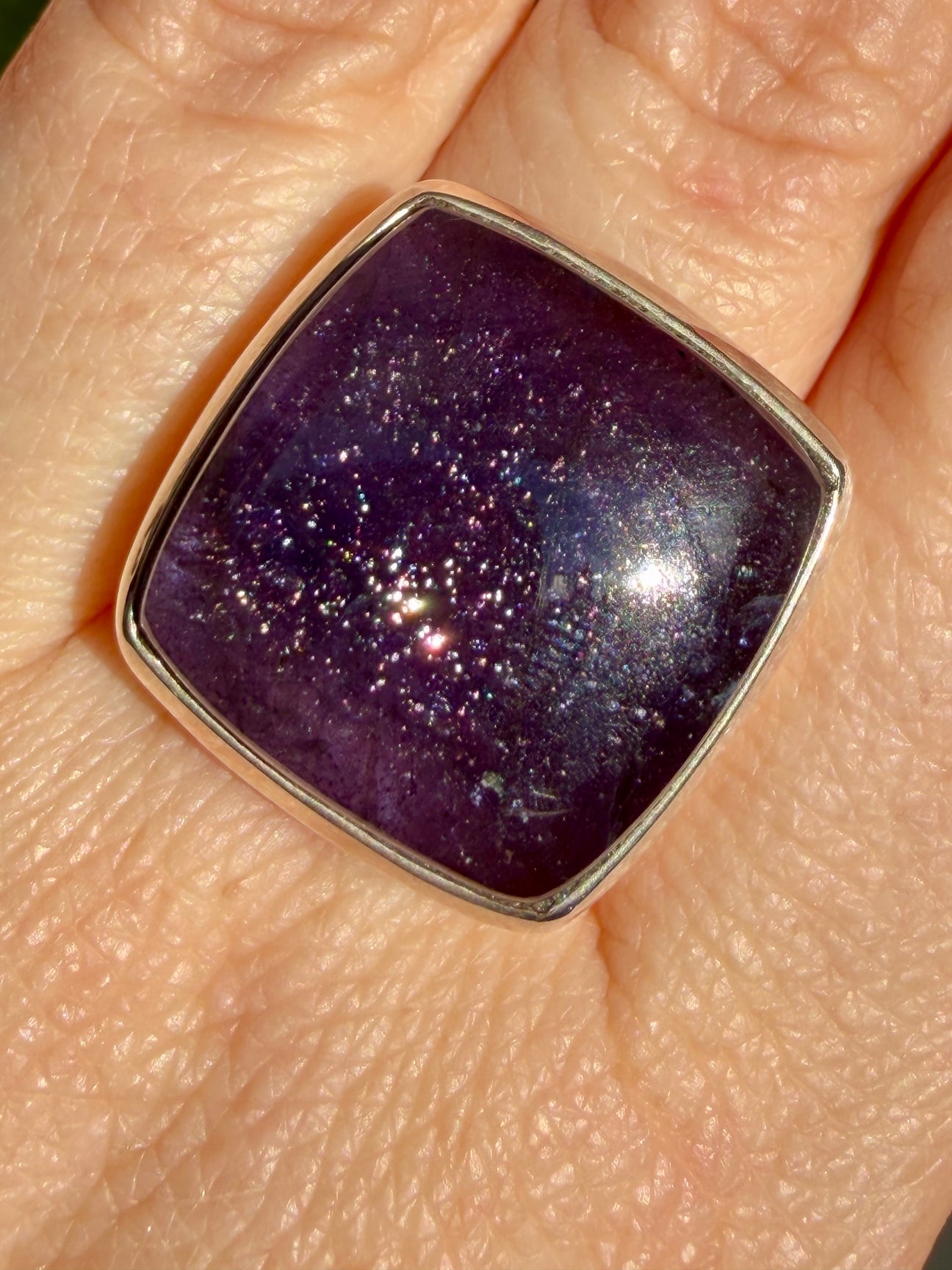 Sunstone in iolite square cushion cabochon ring worn on the hand, showing deep purple-violet colour with dense sparkle concentrated toward the centre