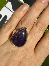 Sunstone in iolite teardrop cabochon ring worn on the hand outdoors, showing deep purple, near-black colour with fine scattered sparkle