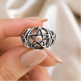 Silver ring with pentagram design on a wooden surface and being worn on a hand.