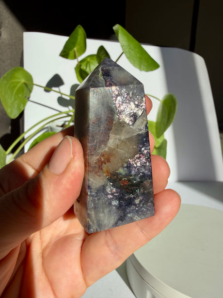 Sunstone in iolite crystal point with a cluster of silver-pink sparkle near the tip and a pale quartz-like pocket lower on the stone