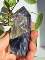 Sunstone in iolite point showing dense pink-copper sparkle through the upper body and a darker indigo-black lower half with a visible fracture line