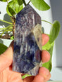 Sunstone in iolite point with a pale smoky-grey inclusion breaking through the sparkling violet upper body, deepening to indigo-blue near the base