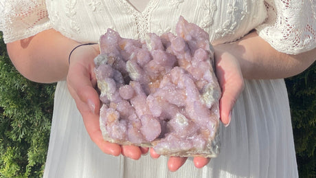 Person holding a cluster of amethyst crystals outdoors with greenery in the background