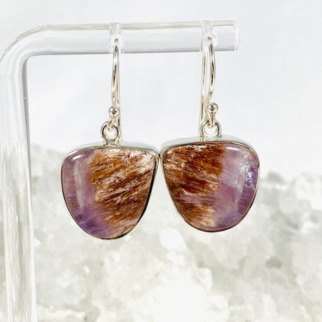 Purple Charoite free form earrings in sterling silver hanging on an earring stand