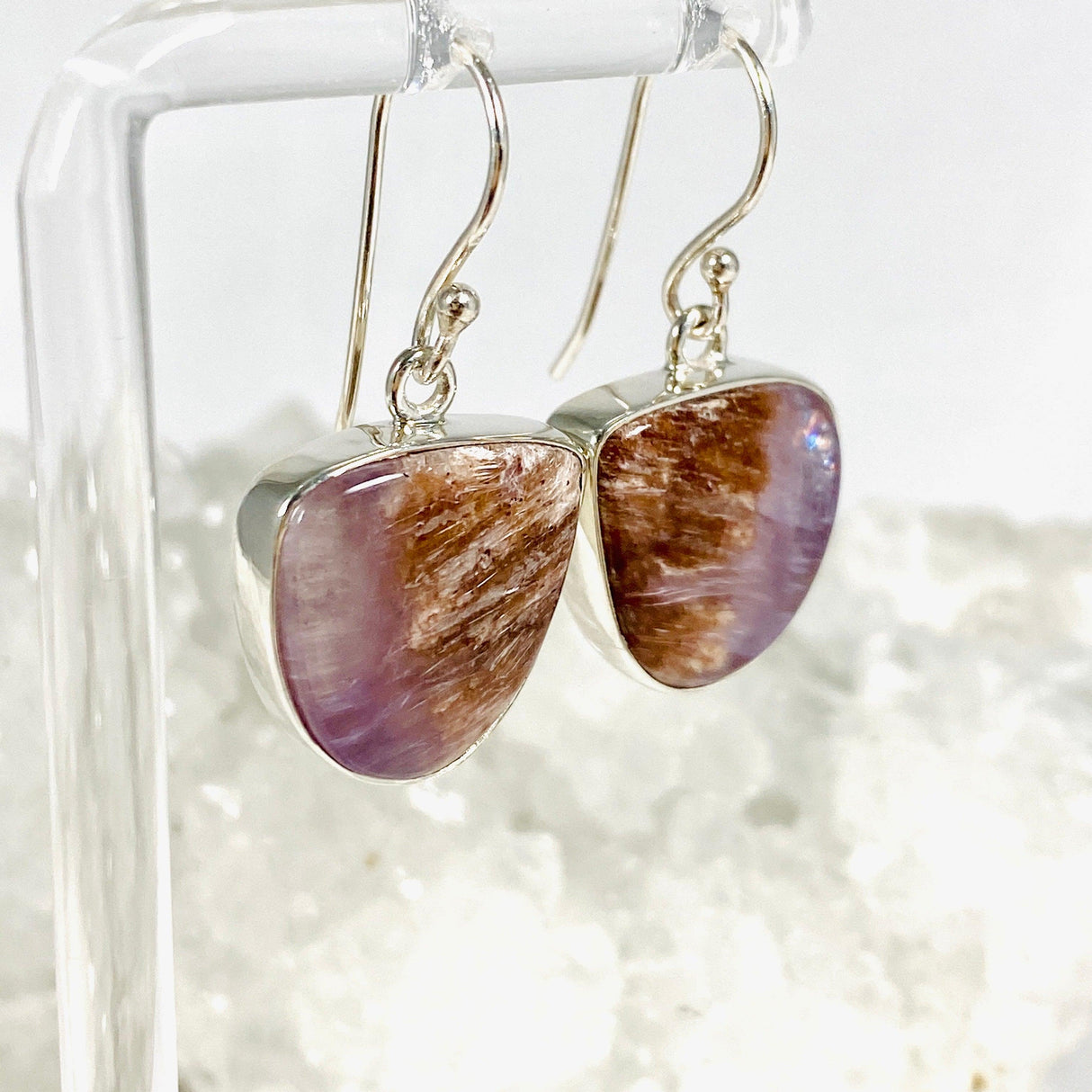 Purple Charoite free form earrings in sterling silver hanging on an earring stand