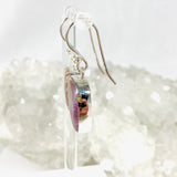 Purple Charoite free form earrings in sterling silver hanging on an earring stand