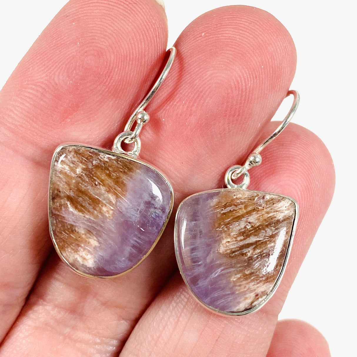 Purple Charoite free form earrings in sterling silver sitting in a hand