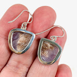 Purple Charoite free form earrings in sterling silver sitting in a hand