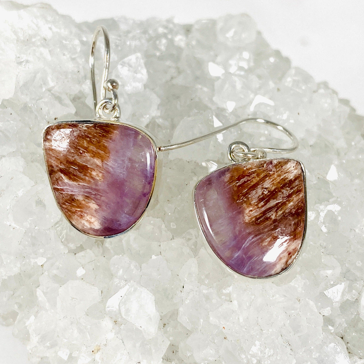 Purple Charoite free form earrings in sterling silver sitting on a crystal cluster