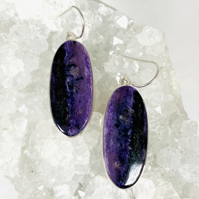 Purple Charoite oval earrings in sterling silver sitting on a crystal cluster