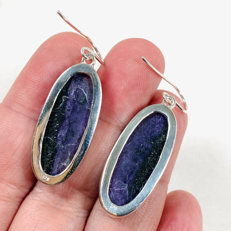 Purple Charoite oval earrings in sterling silver sitting on a hand