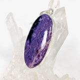 Purple Charoite oval pendant in sterling silver sitting on a crystal cluster