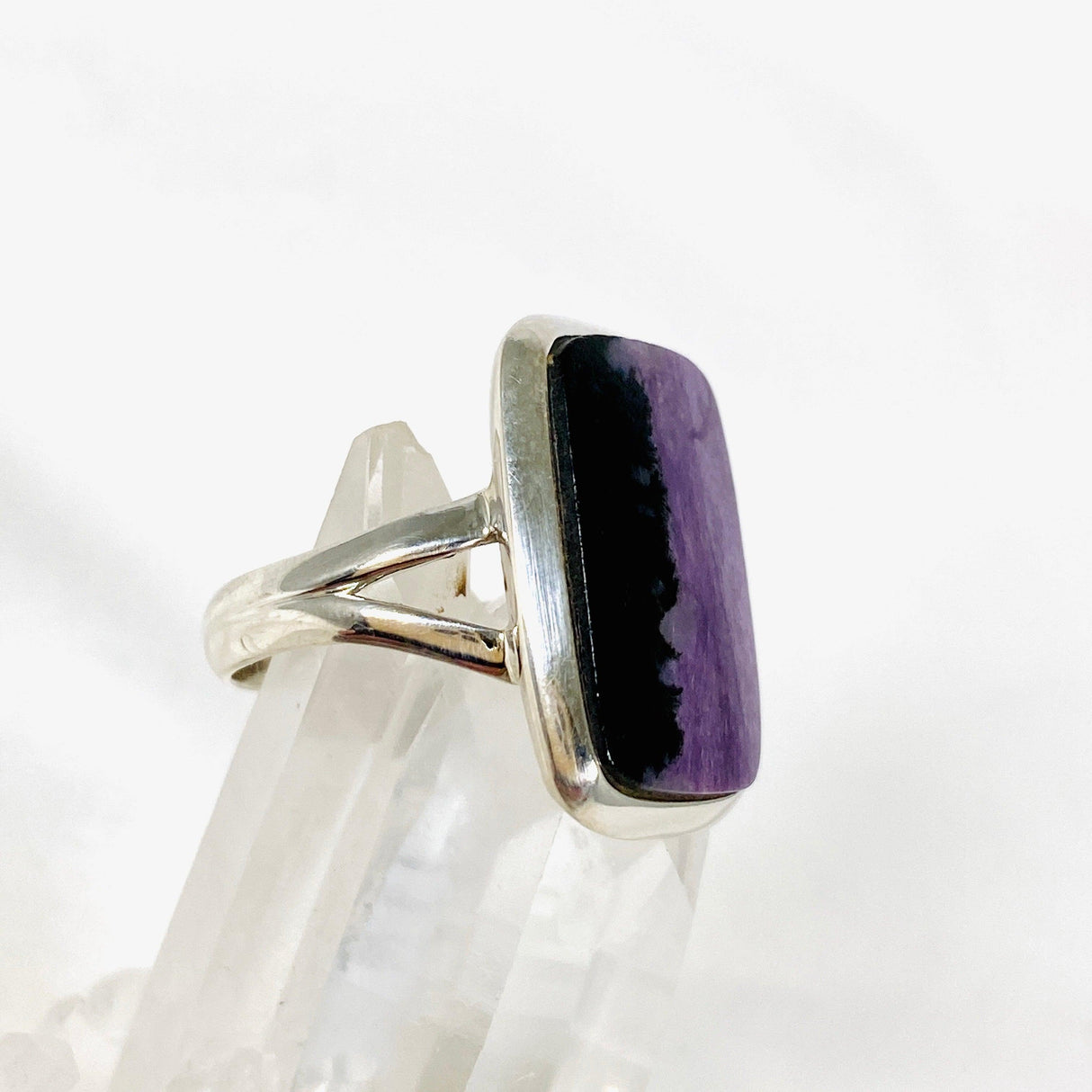 Purple Charoite rectangular ring in sterling silver sitting on a crystal cluster