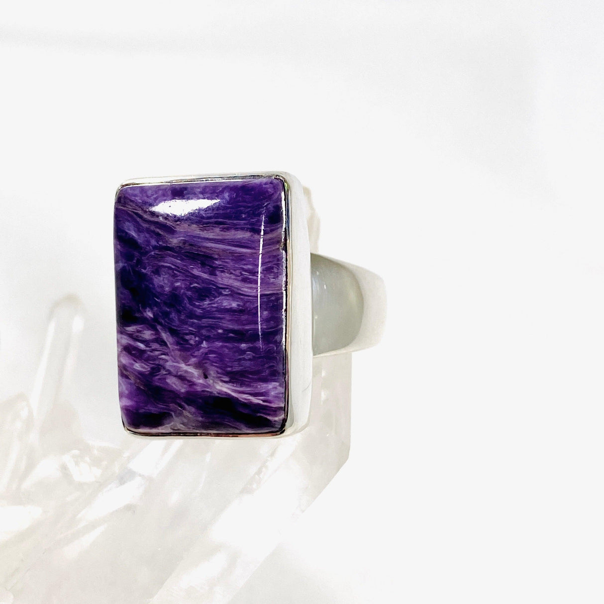 Purple Charoite rectangular ring in sterling silver sitting on a crystal cluster