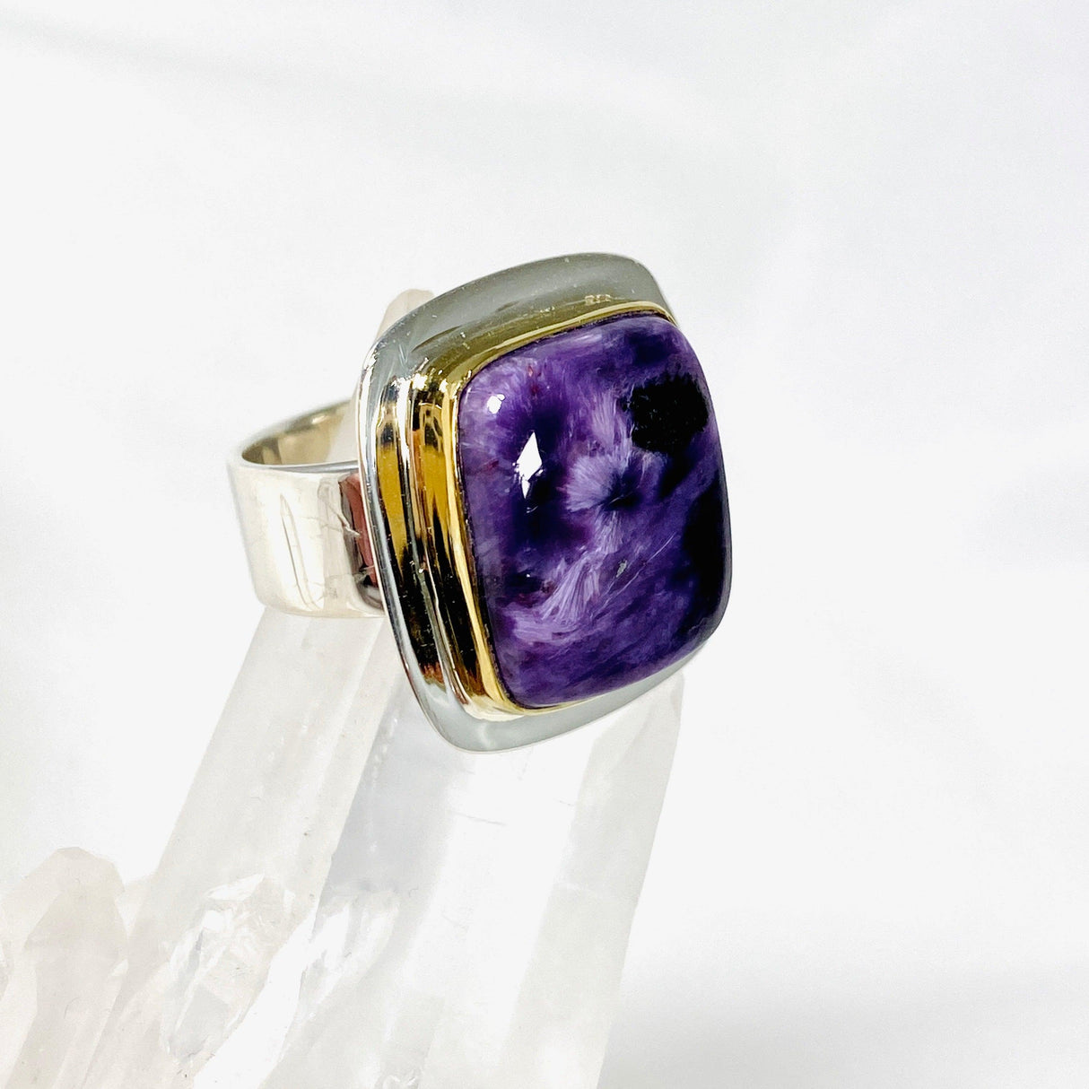 Purple Charoite rectangular ring with brass detailing in sterling silver sitting on a crystal cluster