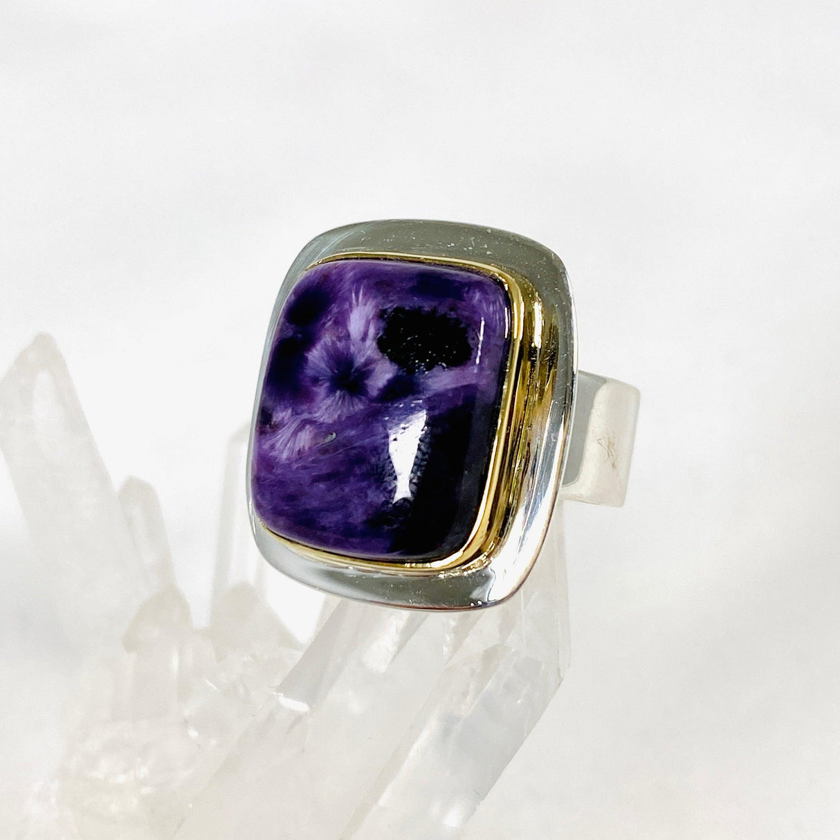 Purple Charoite rectangular ring with brass detailing in sterling silver sitting on a crystal cluster