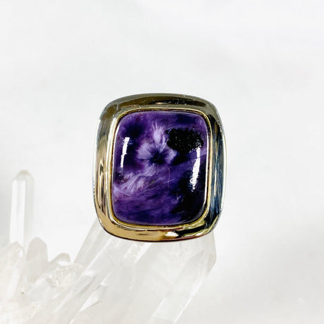 Purple Charoite rectangular ring with brass detailing in sterling silver sitting on a crystal cluster