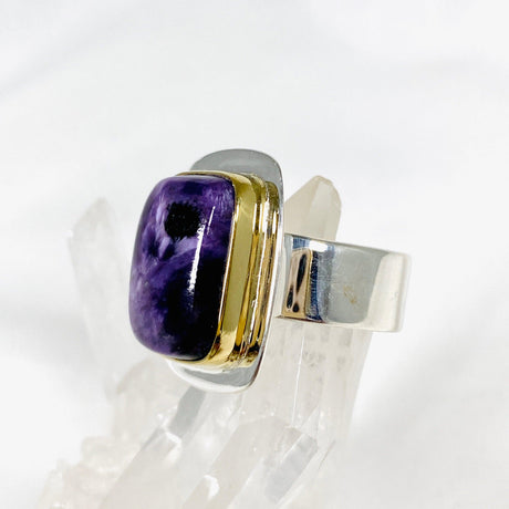 Purple Charoite rectangular ring with brass detailing in sterling silver sitting on a crystal cluster