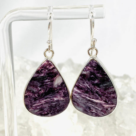Purple Charoite tear drop earrings in sterling silver hanging on an earring stand