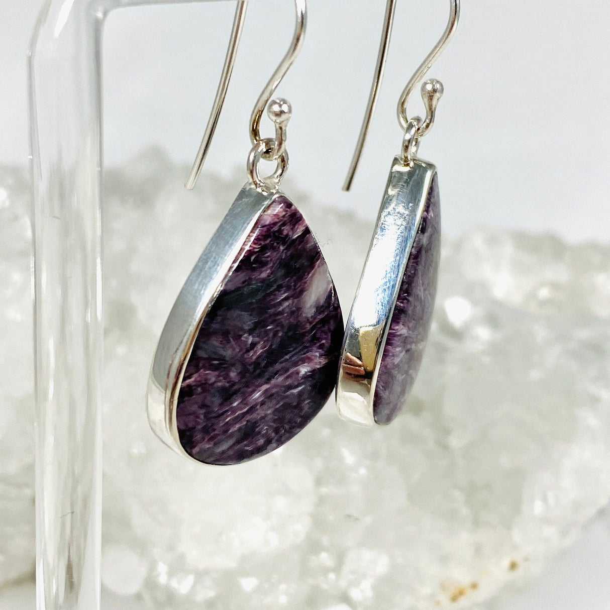 Purple Charoite tear drop earrings in sterling silver hanging on an earring stand